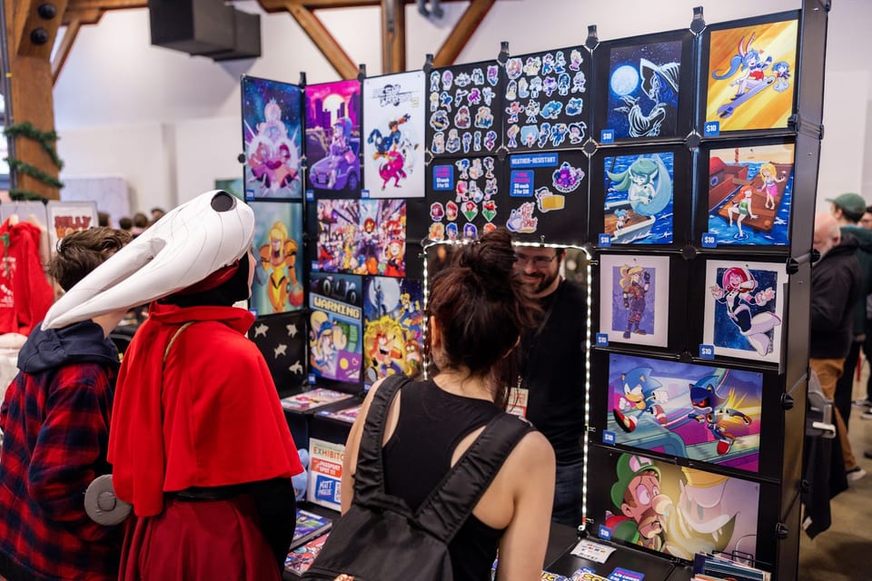 Artist alley booth with prints and cosplayers browsing